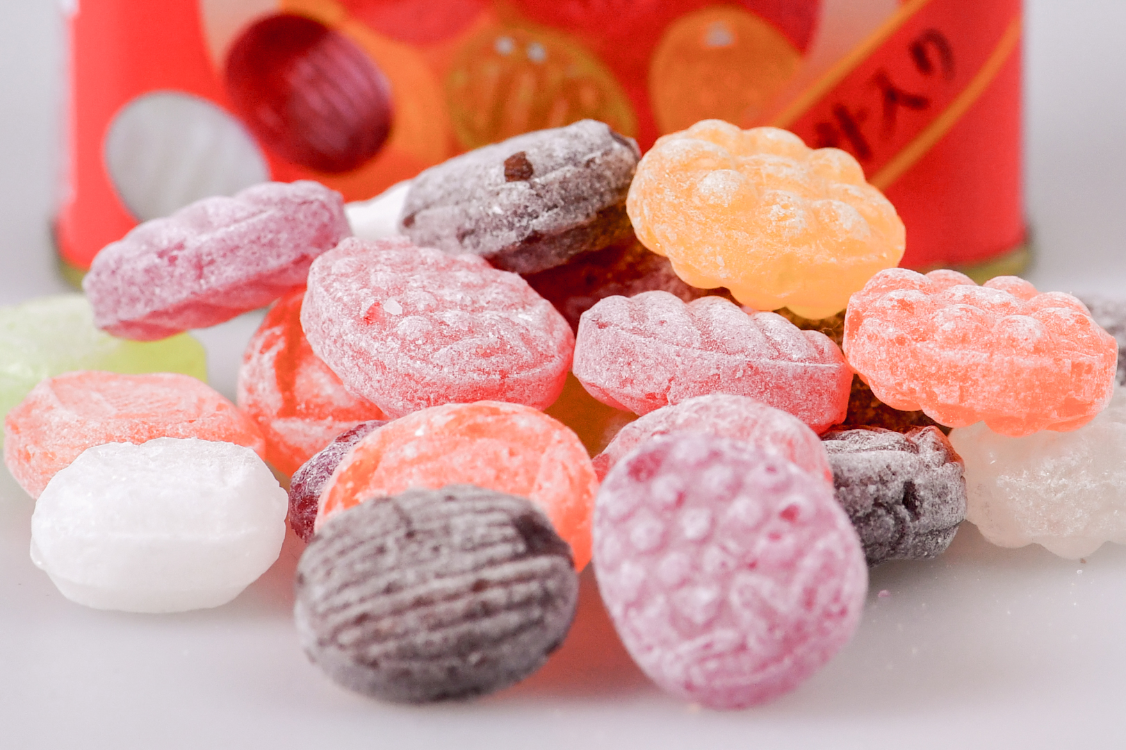 A colorful mix of fruit-flavored hard candies on a white surface with the red metal tin packaging partially in view behind.