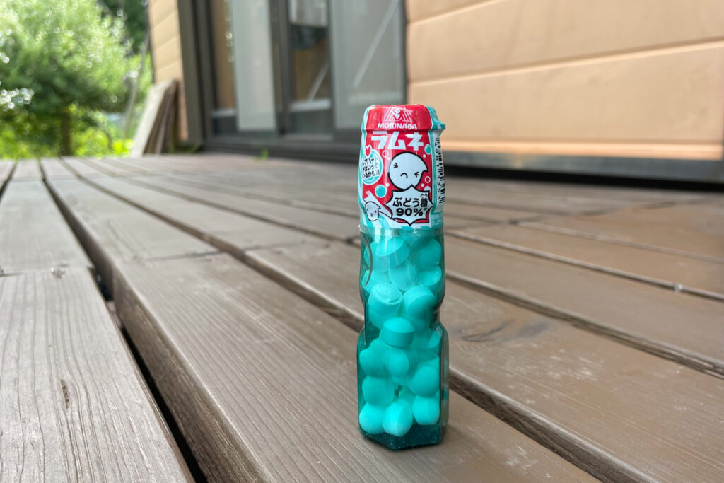 Morinaga Ramune candies. They are packaged in a green-blue bottle that mimics a ramune drink bottle. The photo has been taken outside on a wooden deck.
