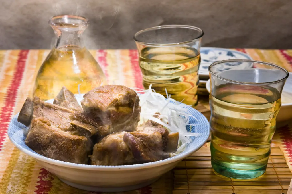 Okinawa drinks: A plate of Okinawan spare ribs with a vessel of local distilled liquor 'Awamori'. There are two glasses also filled with the liquor.