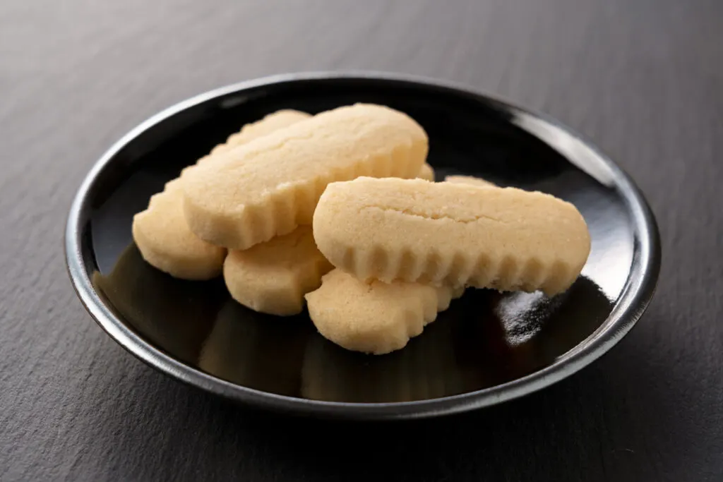 Okinawa food: Five cookies in a finger shape with ribbed sides arranged on a black ceramic plate (these sweets are known as 'chinsuko' in Okinawa).