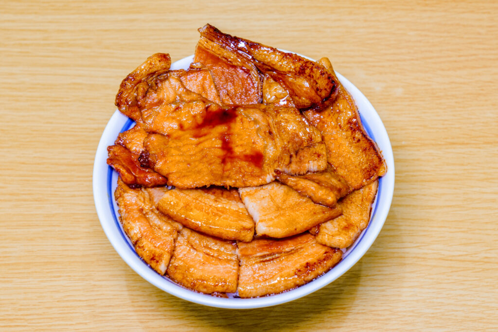 Hokkaido food: A bowl of 'buta don'. The sliced pork is brown from the soy sauce marinade. There are so many slices of pork arranged on top that you cannot see the rice underneath.