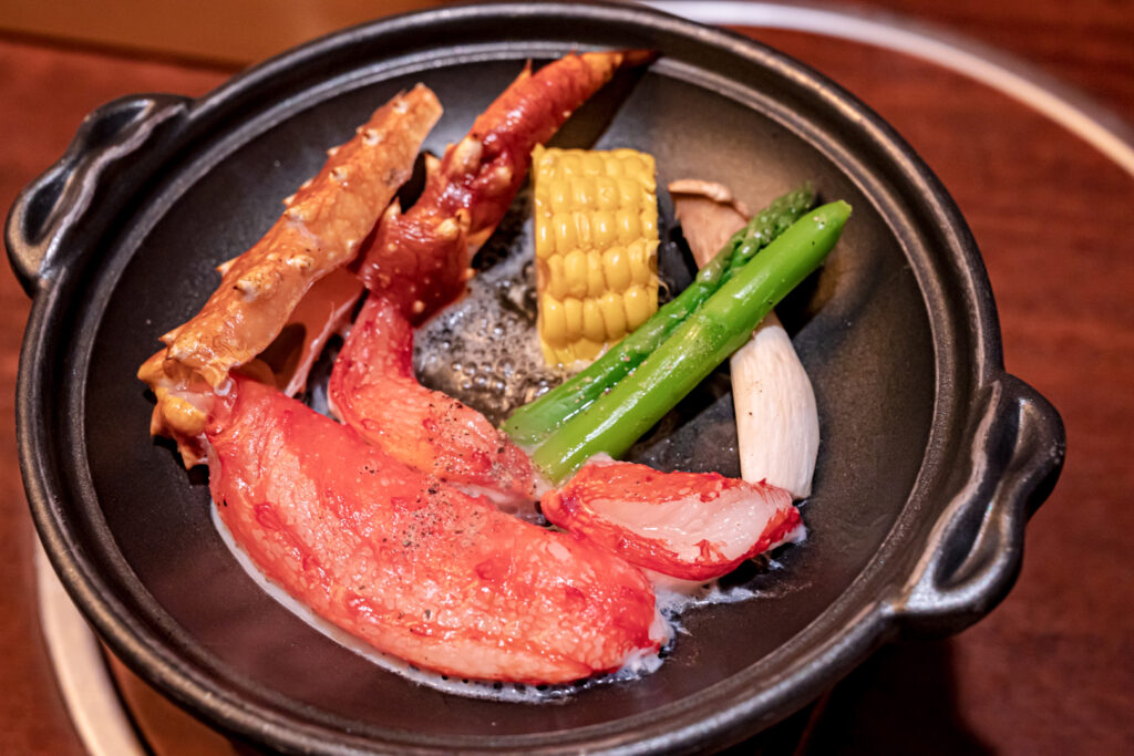 Hokkaido food: Two crab claws on a dark ceramic dish with mushroom, asparagus and corn.