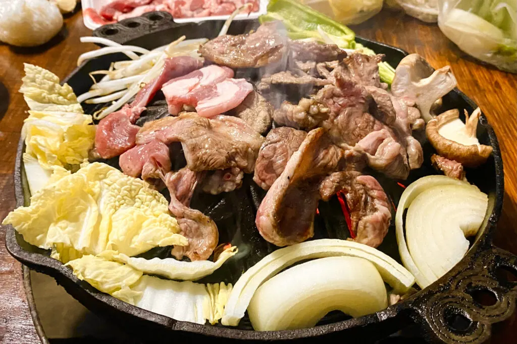 Food in Hokkaido: A tabletop grill with a mound in the center. The thinly-sliced lamb has been arranged over the mound (like a little domed mountain) and vegetables have been placed around the perimeter of the grill. The juices from the lamb run down the mound into the vegetables, infusing them with flavor.