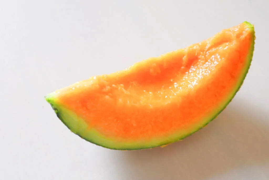 Food in Hokkaido: A large slice of orange-fleshed Yubari melon with the green skin still on and the inner seeds removed.